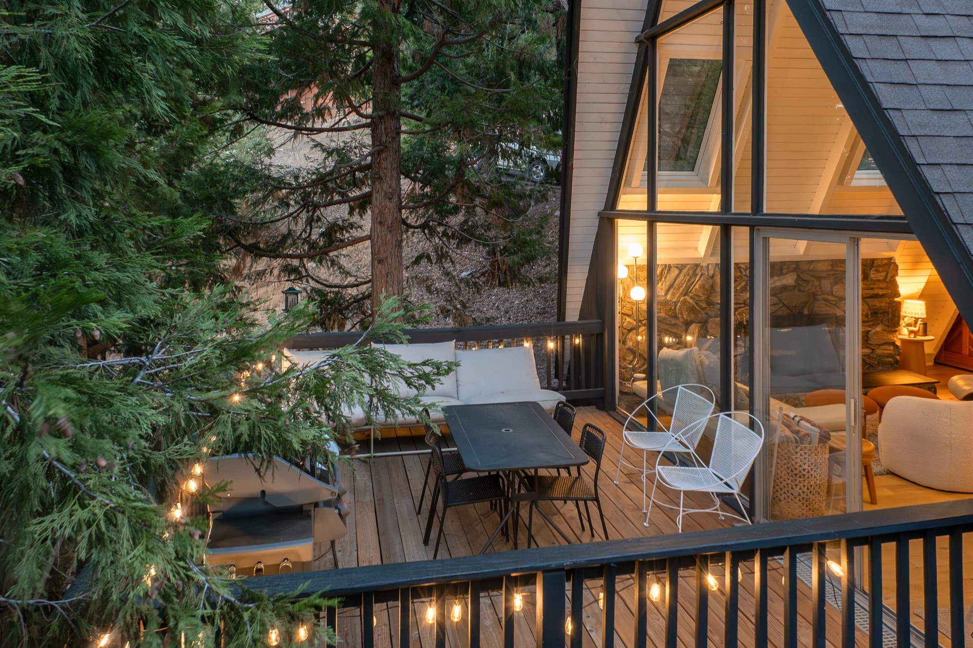 Deck at twilight with string lights, dining table, and A-frame glass wall glowing